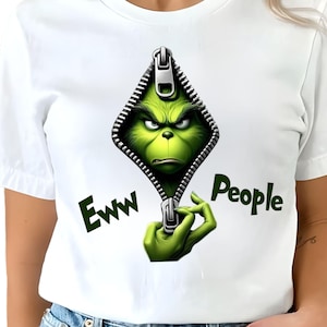 May include: White t-shirt featuring a green Grinch character design. The Grinch is depicted inside a zipper, with the words "Eww People" printed in green. The design is a humorous take on the classic Christmas character.