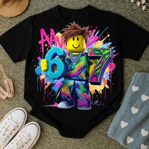 May include: Black t-shirt featuring a colorful graphic of a block figure holding the numbers 6 and 7. The figure has brown hair and a yellow head. The design includes neon paint splatters and the letters "AA".