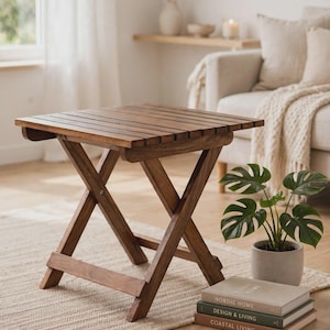 Può includere: Un tavolino pieghevole quadrato in legno con piano a doghe e base a forma di X. Il tavolo è realizzato in legno marrone scuro e presenta un design semplice e funzionale con giunture visibili e una struttura robusta e pieghevole.