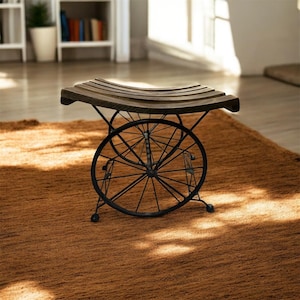 Op de afbeelding: Een decoratieve bank met een donkerhouten zitting en een zwart metalen onderstel. De basis heeft een wielontwerp, wat een unieke, rustieke uitstraling geeft. De bank staat op een bruin tapijt, geschikt voor binnengebruik.