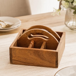May include: A square wooden caddy with a natural brown finish, featuring a central divider and two arched handles with cutout grips. The organiser has a simple, open-top design with visible wood grain, constructed from four sides and a base.