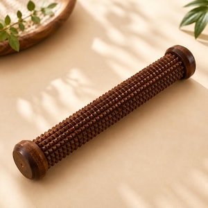 Può includere: Un massaggiatore per piedi cilindrico in legno marrone scuro caratterizzato da una superficie testurizzata coperta da numerose piccole punte. L'attrezzo presenta estremità arrotondate e lisce e una venatura del legno profonda e uniforme.