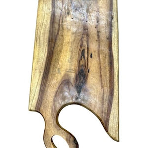 May include: A rectangular wooden chopping board with a natural wood grain. It features a curved handle with a hanging hole. The wood tones vary from light to dark brown, showcasing the natural grain.