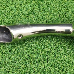 May include: A polished, silver-colored metal tool with a rounded end and a scoop-shaped opening. The tool has a curved handle and is designed for a specific purpose. The object is set against a green background.