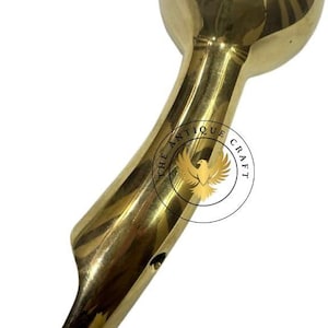 May include: A polished brass handle with a rounded top and a curved, elongated body. The handle features a smooth, reflective surface and is likely a decorative element for furniture or a similar item. The text "THE ANTIQUE CRAFT" is visible.