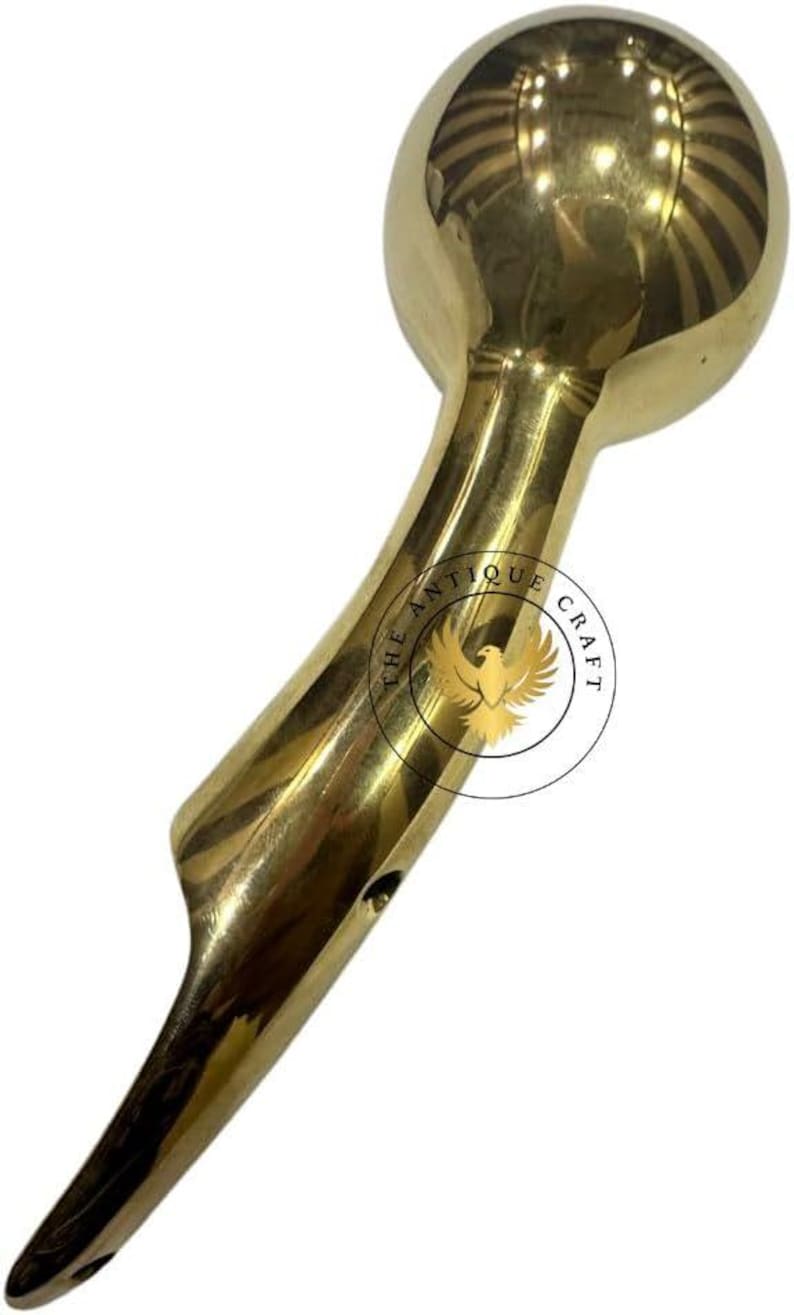 May include: A polished brass handle with a rounded top and a curved, elongated body. The handle features a smooth, reflective surface and is likely a decorative element for furniture or a similar item. The text "THE ANTIQUE CRAFT" is visible.