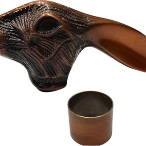 Könnte beinhalten: Ein bronzefarbener, hasenförmiger Griff mit strukturierter Oberfläche und einem separaten zylindrischen Teil. Der Griff weist ein detailliertes Design des Gesichts und der Ohren des Hasen auf. Die Gesamtästhetik ist rustikal und dekorativ.