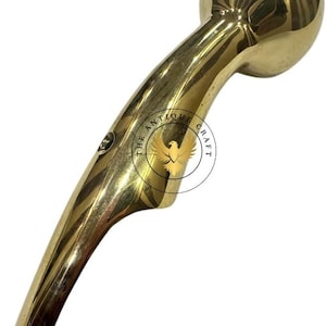May include: A polished brass handle with a rounded top and a curved, ergonomic design. The handle features a small hole at the base and the text "THE ANTIQUE CRAFT" around a bird emblem. This item is likely a decorative or functional hardware piece.