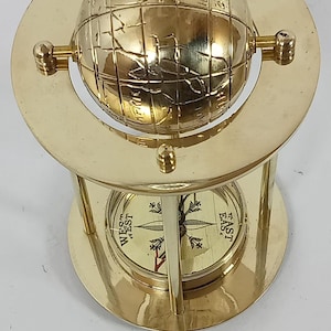 May include: A brass compass with a globe design. The globe is mounted on a brass stand with a compass rose at the base. The compass rose indicates directions such as West and East.