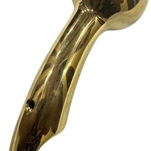 Könnte beinhalten: Goldfarbener Handbrausekopf mit rundem Oberteil und gebogenem Griff. Der Duschkopf hat eine glatte, reflektierende Oberfläche und ein kleines Loch in der Nähe des Griffansatzes. Das Design ist elegant und modern.