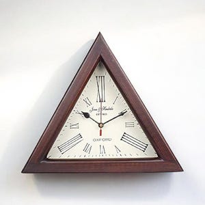 May include: A triangular wall clock with a dark brown wooden frame. The clock face is off-white with black Roman numerals and hands. The clock has the text "Jane Hendrix Oxford" on the face.