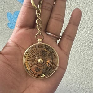 May include: A vintage brass perpetual calendar keyring. The round calendar features engraved text and a central dial. The keyring includes a clasp and chain. The calendar displays the years and months.