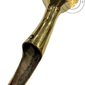 May include: A vintage brass door handle with a rounded top and a long, open handle. The handle has a polished finish and shows signs of age and wear. The Antique Craft logo is visible.