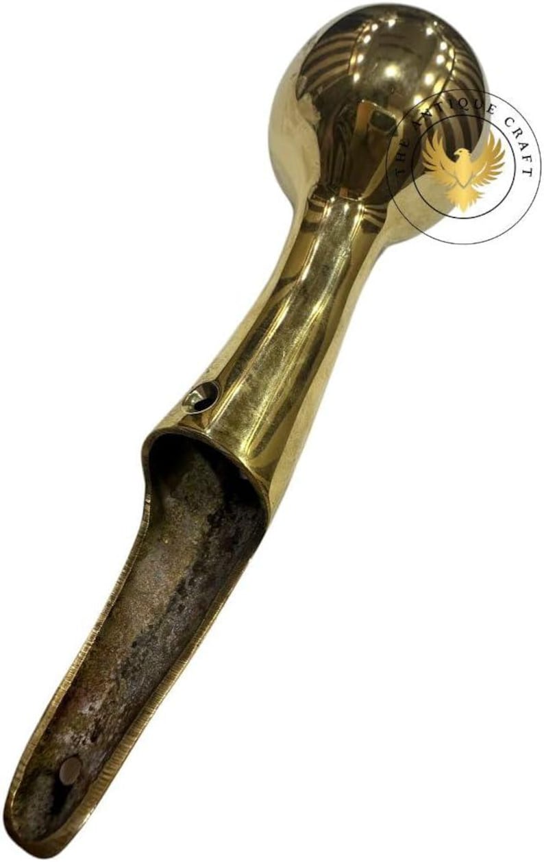 May include: A vintage brass door handle with a rounded top and a long, open handle. The handle has a polished finish and shows signs of age and wear. The Antique Craft logo is visible.