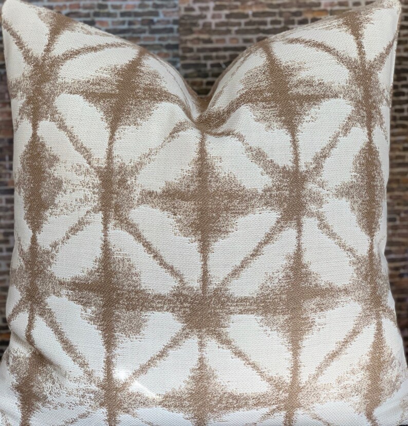 May include: A white throw pillow with a geometric pattern in brown. The pattern is made up of overlapping diamonds and stars.