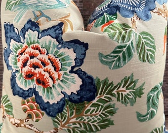 Peut inclure: Un coussin décoratif à motif floral. Le coussin présente de grandes fleurs stylisées dans des tons de bleu, d'orange et de blanc sur un fond vert clair. Des feuilles vertes et des tiges brunes complètent le design. Le coussin est de forme carrée.