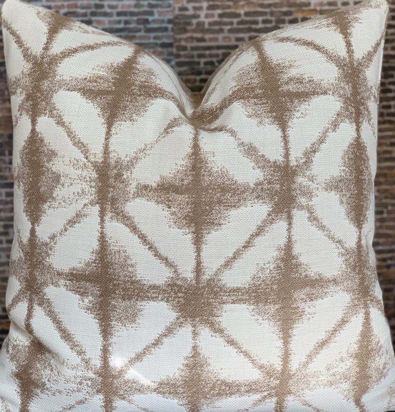May include: A white throw pillow with a geometric pattern in brown. The pattern is made up of overlapping diamonds and stars.