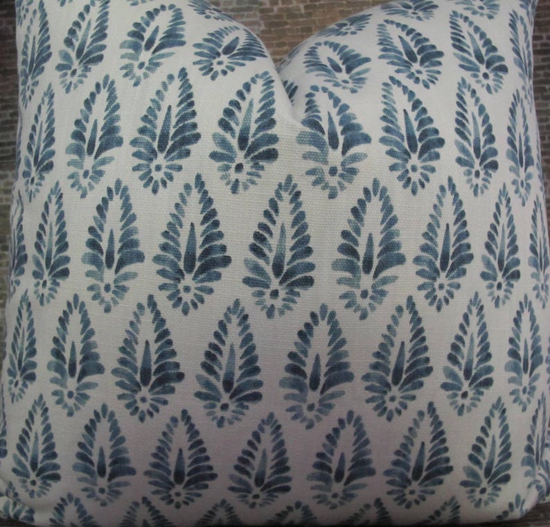Puede incluir: Coj&iacute;n cuadrado decorativo con fondo blanco y un patr&oacute;n repetido de dise&ntilde;os florales azules en forma de l&aacute;grima. La almohada tiene un aspecto suave y texturizado, lo que sugiere un art&iacute;culo de decoraci&oacute;n del hogar.