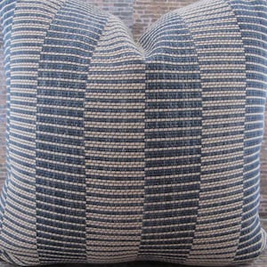 May include: Square decorative pillow with a woven pattern of alternating vertical stripes in navy blue and beige. The pillow has a soft, textured appearance, suitable for home decor.