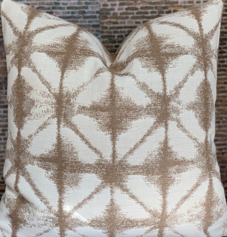 May include: A white throw pillow with a geometric pattern in brown. The pattern is made up of overlapping diamonds and stars.