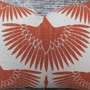 Op de afbeelding: Een decoratief kussen met een roestkleurig ontwerp van gestileerde vogels met uitgespreide vleugels. Het kussen is gemaakt van natuurlijke linnen stof.