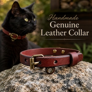 Può includere: Un collare in vera pelle rosso scuro con fibbia in ottone e un piccolo anello metallico per una medaglietta. Il testo "Handmade Genuine Leather Collar" è visibile in alto a destra. Il collare presenta due rivetti in ottone.