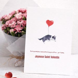 Puede incluir: Tarjeta de San Valentín con una ilustración en acuarela de un gato blanco y negro flotando con un globo rojo en forma de corazón. La tarjeta tiene el texto: "De la première rencontre à aujourd'hui : je t'aime. Joyeuse Saint Valentin."