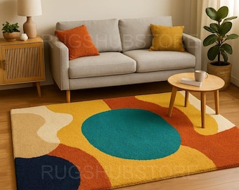 May include: A colorful abstract area rug with a geometric design. The rug features a large teal circle surrounded by orange, yellow, beige, and navy blue shapes. The rug is placed in front of a gray sofa.
