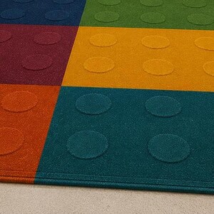 May include: A rectangular area rug featuring a grid of six large colored squares in blue, green, maroon, yellow, orange, and teal. Each square contains a raised circular pattern, creating a textured surface that resembles a building block toy.