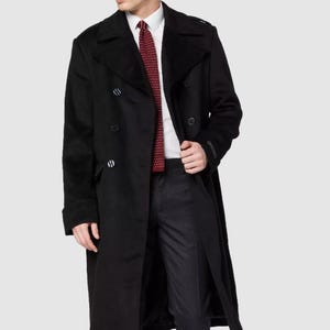 May include: A black overcoat with a double-breasted design. The coat features a notched collar, button closures, and a long length. The person is wearing a white shirt and a red patterned tie, with dark gray pants and black shoes.