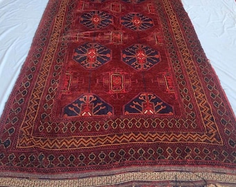 May include: A rectangular area rug featuring a deep red background with repeating dark blue geometric medallions and intricate border patterns. The rug includes a fringe along the bottom edge, showcasing a traditional woven design with symmetrical motifs.
