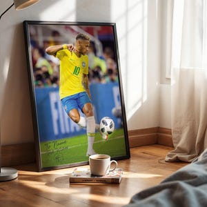 Pode incluir: Impress&atilde;o emoldurada de um jogador de futebol com uma camisa amarela, n&uacute;mero 10, chutando uma bola de futebol. A impress&atilde;o &eacute; assinada e inclui o texto "To Name Best Wishes". Uma x&iacute;cara de caf&eacute; e um livro est&atilde;o em frente &agrave; impress&atilde;o.
