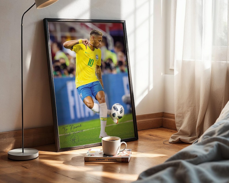 Pode incluir: Impress&atilde;o emoldurada de um jogador de futebol com uma camisa amarela, n&uacute;mero 10, chutando uma bola de futebol. A impress&atilde;o &eacute; assinada e inclui o texto "To Name Best Wishes". Uma x&iacute;cara de caf&eacute; e um livro est&atilde;o em frente &agrave; impress&atilde;o.