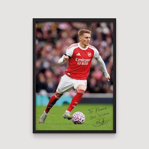 May include: Framed print of a soccer player in a red and white jersey, kicking a purple and white soccer ball on a green field. The jersey has the "Emirates Fly Better" logo. The print includes the text "To Name Best Wishes" and a signature.