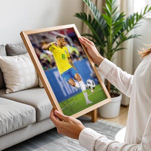 Pode incluir: Uma impress&atilde;o emoldurada com um jogador de futebol com uma camisa amarela e cal&ccedil;&otilde;es azuis a chutar uma bola num campo verde. A impress&atilde;o est&aacute; numa moldura de madeira castanha clara. O texto "To Name" &eacute; vis&iacute;vel na parte inferior esquerda.