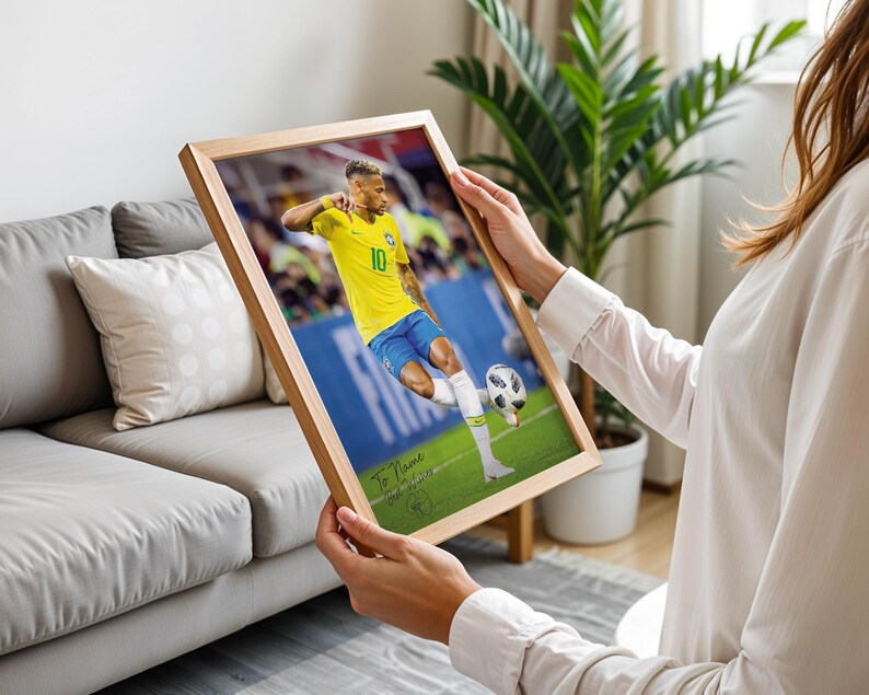 Pode incluir: Uma impress&atilde;o emoldurada com um jogador de futebol com uma camisa amarela e cal&ccedil;&otilde;es azuis a chutar uma bola num campo verde. A impress&atilde;o est&aacute; numa moldura de madeira castanha clara. O texto "To Name" &eacute; vis&iacute;vel na parte inferior esquerda.