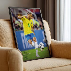 Pode incluir: Impress&atilde;o emoldurada de um jogador de futebol com uma camisa amarela com o n&uacute;mero 10, chutando uma bola de futebol em um campo verde. A impress&atilde;o est&aacute; em uma moldura preta e repousa em uma poltrona bege.