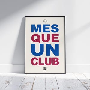 May include: Framed poster with the text "MES QUE UN CLUB" in blue and maroon, with a soccer ball and crest icon. The poster is displayed against a white wall and a wooden floor.