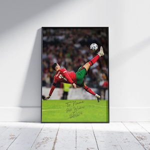Puede incluir: Impresi&oacute;n enmarcada de un futbolista con uniforme rojo y verde pateando un bal&oacute;n en el aire. La imagen est&aacute; ambientada en un fondo de estadio borroso. La impresi&oacute;n incluye el texto "To Name Best Wishes" y una firma.