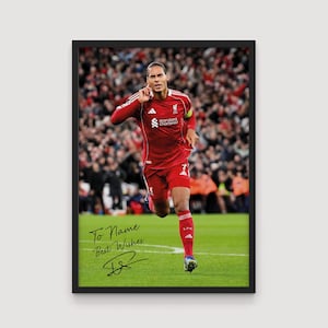 Puede incluir: Impresión enmarcada de un jugador de fútbol con uniforme rojo, corriendo sobre un campo verde. El jugador celebra con el brazo levantado. La impresión incluye el texto "To Name Best Wishes" y una firma.