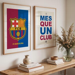 May include: Two framed art prints featuring FC Barcelona branding. One print displays the team's crest with the text "FC Barcelona" below. The other print has the text "MES QUE UN CLUB" in blue and red.
