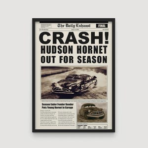 Op de afbeelding: Een ingelijste sepia-getinte afdruk van een krantenpagina. De kop luidt "CRASH! HUDSON HORNET OUT FOR SEASON." Afbeeldingen van een vintage raceauto zijn te zien. De print zit in een zwart frame.