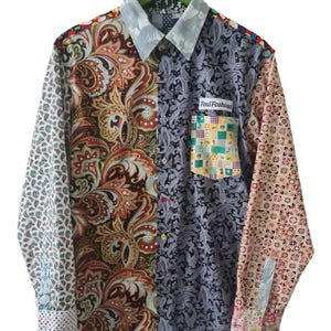 Pode incluir: Uma camisa de manga comprida com botões e um design de patchwork com vários padrões, incluindo paisley, formas geométricas e bolinhas. A camisa tem um bolso no peito com o texto Foul Fashion e uma gola azul clara com estampa floral.