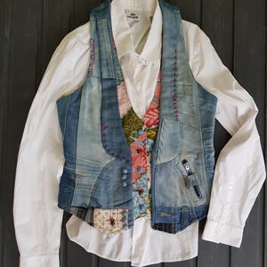 Può includere: Un gilet di jeans con un design patchwork sopra una camicia bianca button-down. Il gilet presenta una varietà di lavaggi di denim, cuciture decorative e un pannello di tessuto fantasia. La camicia ha un logo Lacoste.