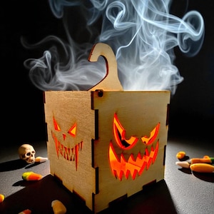 May include: A wooden Halloween box with carved jack-o'-lantern faces. The box glows orange from within, and smoke rises from the top. A small skull and candy corn are scattered around the base.