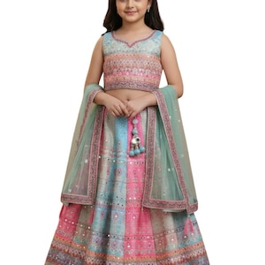 May include: A vibrant, traditional Indian outfit for a young girl. The ensemble features a patterned top, a long skirt, and a sheer, mint green scarf. The skirt and top incorporate pink, blue, and silver detailing.