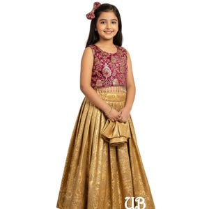Pode incluir: Um vestido formal dourado e bordô para uma menina. A parte superior sem mangas é bordô com bordados florais dourados. A saia é dourada com um padrão texturizado. Um laço a condizer está no cabelo da menina. O vestido tem uma bolsa dourada a condizer.