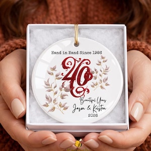 May include: A round white ceramic ornament in a gift box featuring the text Hand in Hand Since 1986, a large red script number 40, botanical illustrations, and the text Beautiful Years Jason & Kristen 2026 with a gold hanging string.