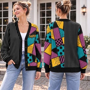 May include: A long-sleeve V-neck cardigan featuring a black and white pinstripe pattern on one side and a colorful patchwork design on the other. The patchwork includes yellow, purple, and teal squares with polka dots and spiderweb motifs. The name Sophia is embroidered in yellow on the chest.