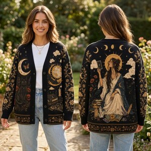 May include: A black knit cardigan featuring a button-front closure and intricate gold and cream celestial designs. The front displays a crescent moon, a cat, and floral motifs. The back depicts a figure holding a tarot card with a raven.